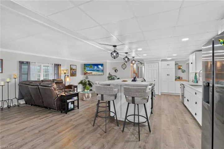 Open-concept living area featuring wood-finish flooring, a kitchen island with seating, white cabinetry, stainless steel appliances, and recessed lighting