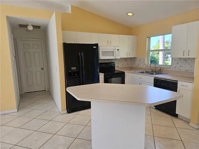 Kitchen with sink, decorative backsplash, light tile patterned floors, black appliances, and lofted ceiling
