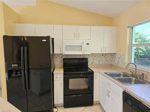 Kitchen with light tile patterned flooring, backsplash, sink, vaulted ceiling, and black appliances