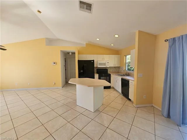 Kitchen with backsplash, a center island, lofted ceiling, black appliances, and white cabinets