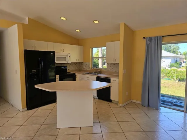 Kitchen with plenty of natural light, black appliances, backsplash, and lofted ceiling