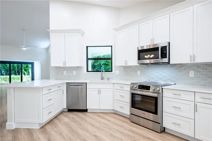 Kitchen with white cabinets, light hardwood / wood-style flooring, decorative backsplash, appliances with stainless steel finishes, and kitchen peninsula