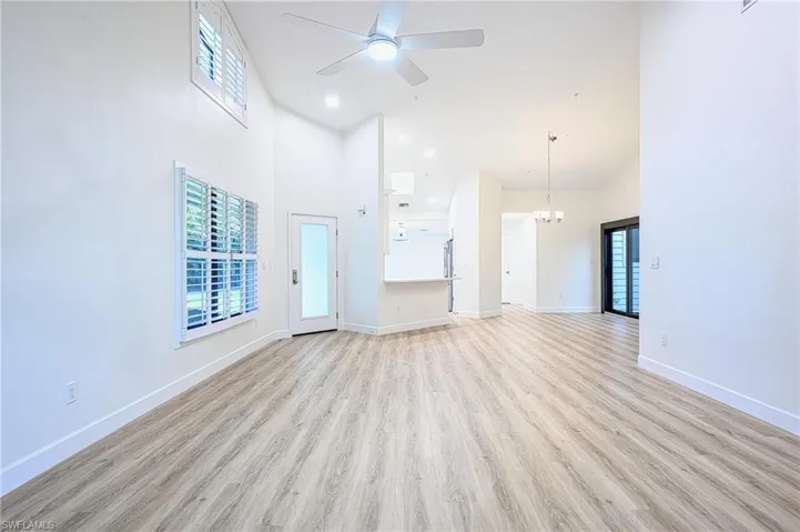Unfurnished living room featuring ceiling fan with notable chandelier, light hardwood / wood-style floors, and a high ceiling