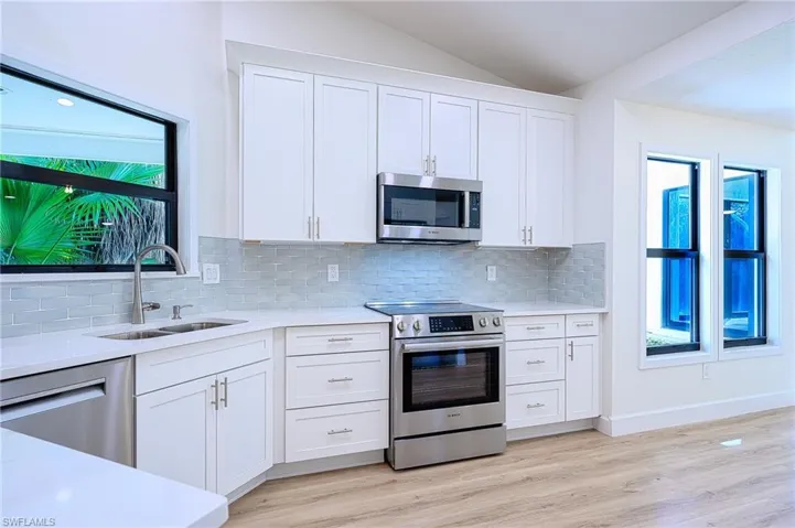 Kitchen with sink, vaulted ceiling, appliances with stainless steel finishes, light hardwood / wood-style floors, and white cabinetry