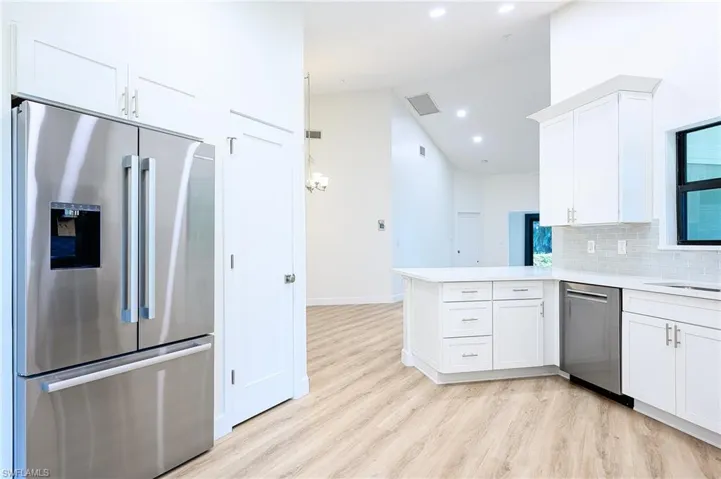Kitchen with kitchen peninsula, appliances with stainless steel finishes, tasteful backsplash, light hardwood / wood-style flooring, and white cabinets