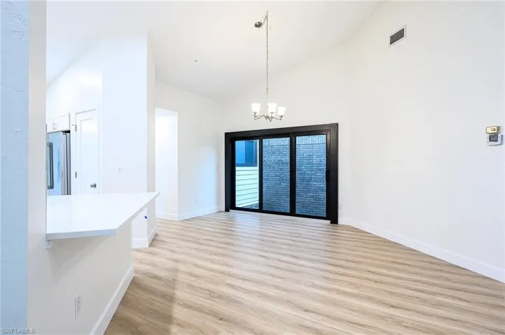 Unfurnished dining area featuring high vaulted ceiling, a chandelier, and light wood-type flooring