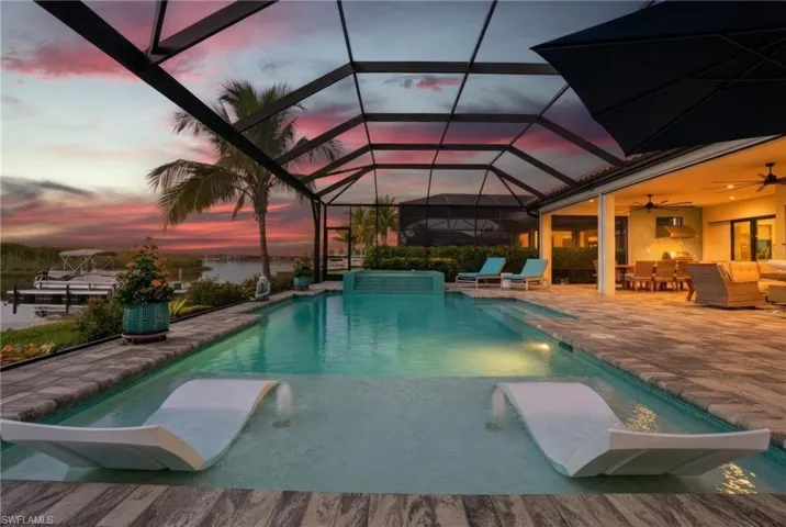 Pool at dusk featuring a sunroom, a patio, glass enclosure, a pool with connected hot tub, and a water view