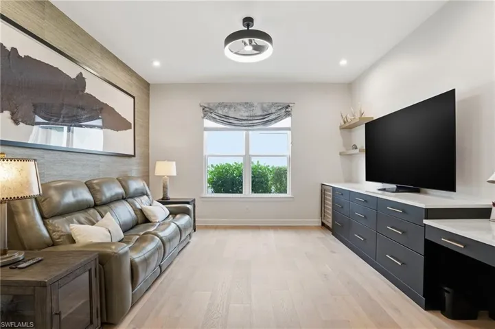 Living room with an accent wall, light wood finished floors, beverage cooler, and recessed lighting