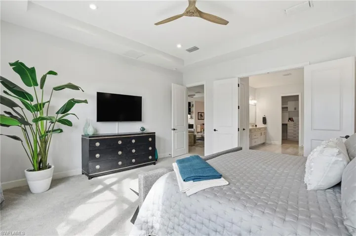 Bedroom featuring carpet floors, ceiling fan, recessed lighting, ensuite bathroom, and a tray ceiling