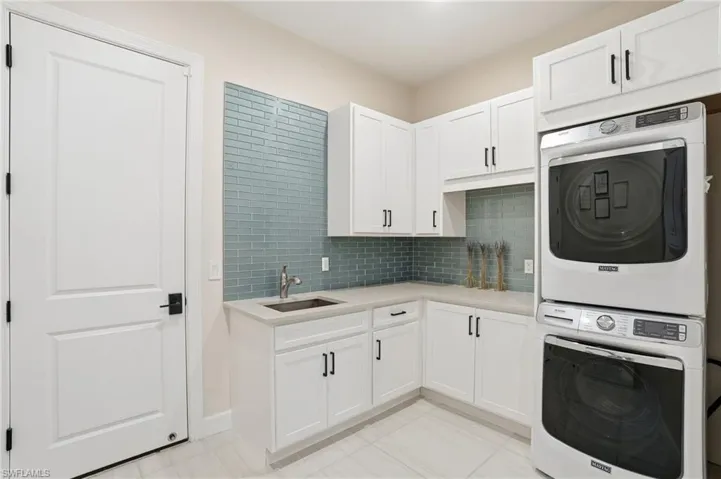 Kitchen featuring white cabinetry, tasteful backsplash, stacked washer / dryer, light stone counters, and light tile patterned floors