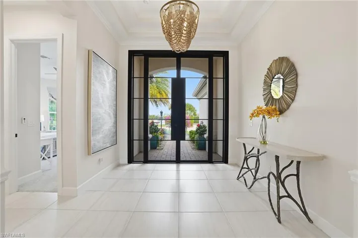 Tiled foyer featuring healthy amount of natural light, a chandelier, ornamental molding, french doors, and a tray ceiling