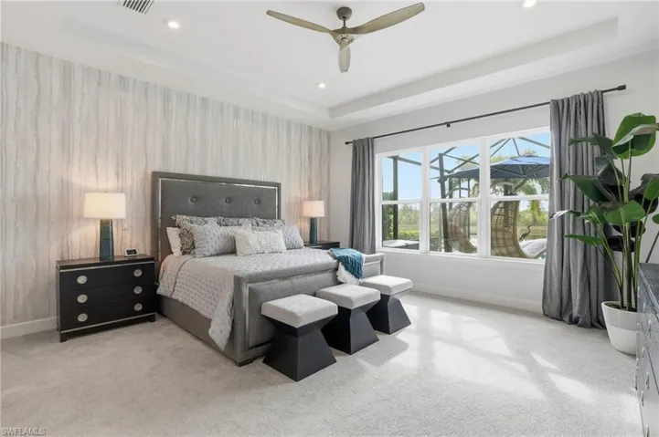 Bedroom featuring a tray ceiling, wallpapered walls, light carpet, ceiling fan, and an accent wall