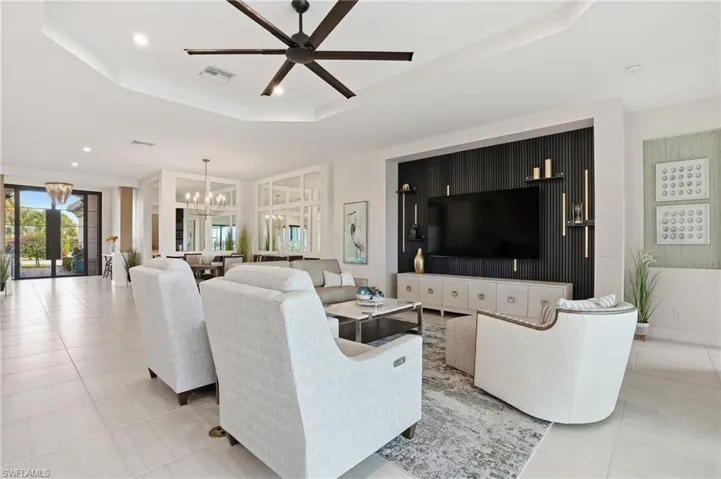 Living room with a tray ceiling, recessed lighting, tile patterned flooring, a chandelier, and a ceiling fan