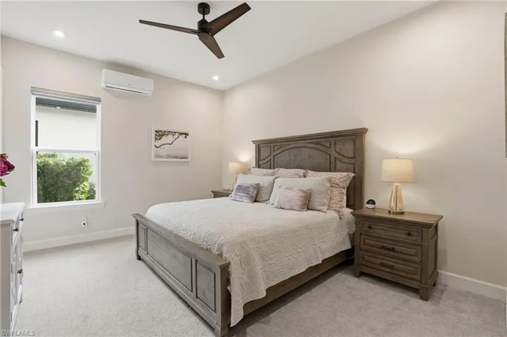 Bedroom featuring light colored carpet, a ceiling fan, and a wall mounted AC