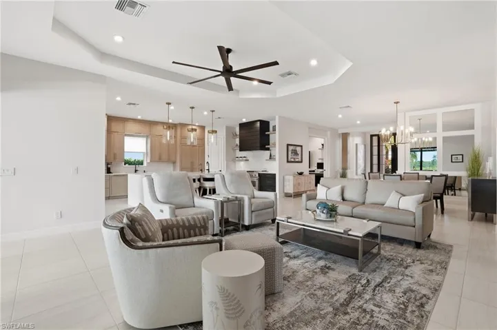 Living room with a chandelier, a ceiling fan, a tray ceiling, recessed lighting, and light tile patterned flooring
