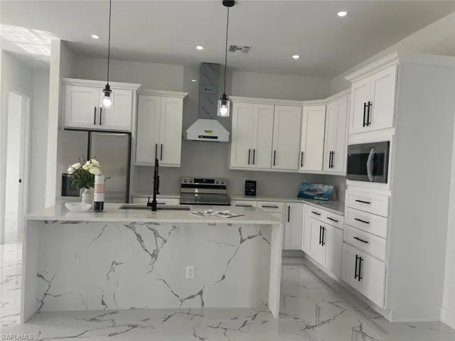 Kitchen with hanging light fixtures, wall chimney range hood, white cabinetry, and stainless steel appliances