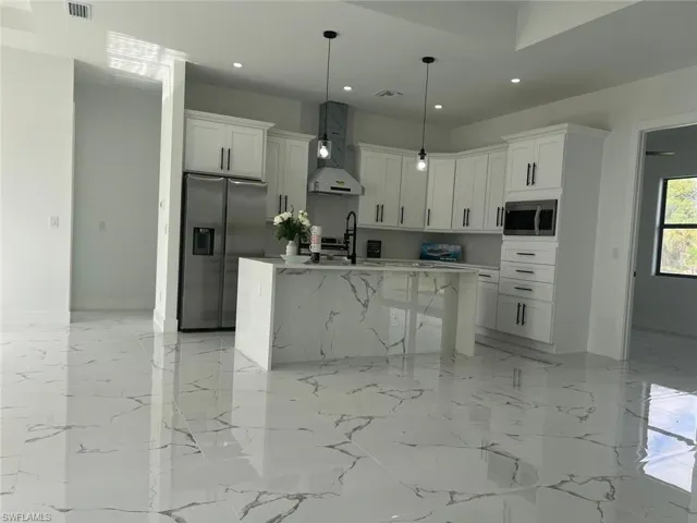 Kitchen with a kitchen island with sink, wall chimney exhaust hood, white cabinets, and stainless steel appliances
