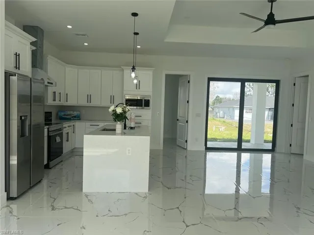 Kitchen featuring white cabinets, wall chimney exhaust hood, appliances with stainless steel finishes, light countertops, and pendant lighting