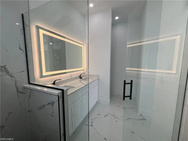Full bath featuring marble finish floor, double vanity, a sink, and a marble finish shower