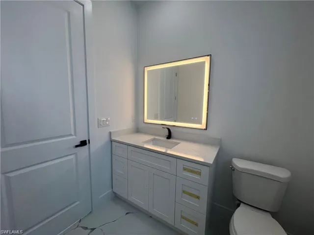 Bathroom featuring toilet, marble finish floor, and vanity