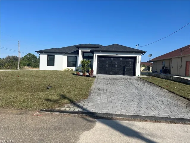 Prairie-style home with a front lawn, decorative driveway, an attached garage, and stucco siding