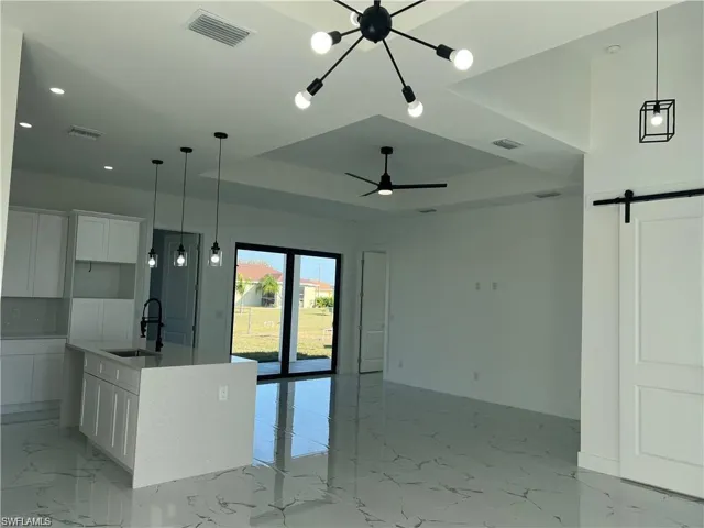 Kitchen with a tray ceiling, a barn door, white cabinetry, a sink, and an island with sink