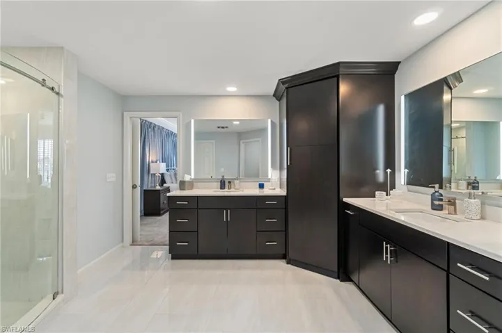 Full bathroom with a shower stall, two vanities, light tile patterned floors, and recessed lighting