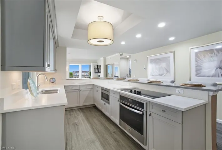 Kitchen with a peninsula, appliances with stainless steel finishes, light wood-type flooring, recessed lighting, and a raised ceiling