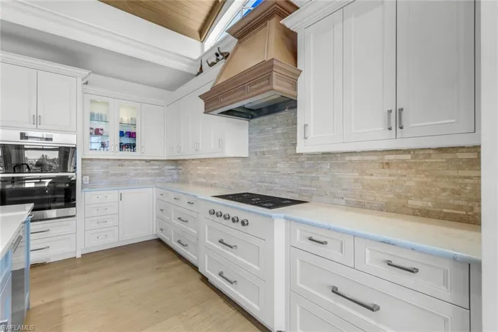 Kitchen featuring tasteful backsplash, white cabinetry, glass insert cabinets, appliances with stainless steel finishes, and custom exhaust hood