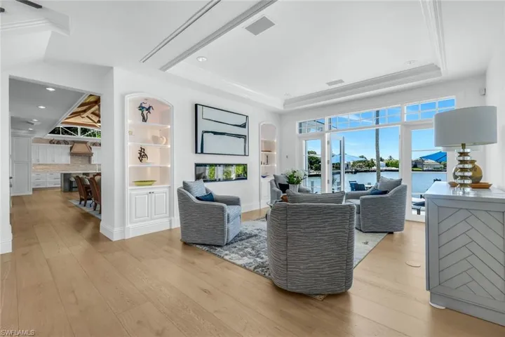 Living room featuring light wood-style flooring, a water view, built in features, a fireplace, and ornamental molding