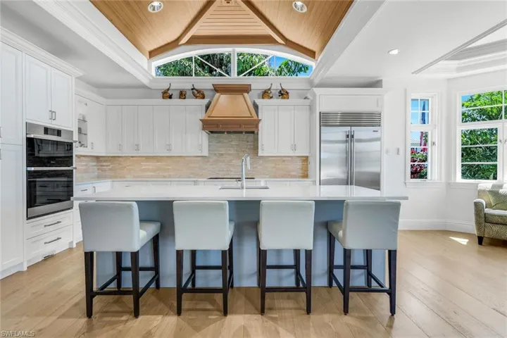 Kitchen with vaulted ceiling, decorative backsplash, appliances with stainless steel finishes, an island with sink, and white cabinetry
