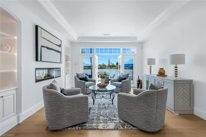 Living area with a water view, light wood-type flooring, crown molding, and a raised ceiling