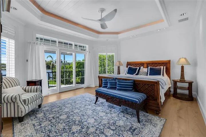 Bedroom featuring light wood-style flooring, access to outside, a tray ceiling, crown molding, and a ceiling fan