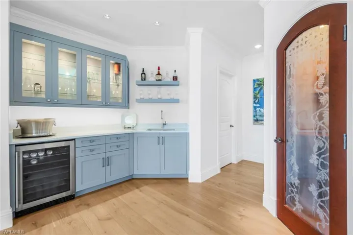 Indoor wet bar with open shelves, glass insert cabinets, beverage cooler, light wood-style floors, and ornamental molding