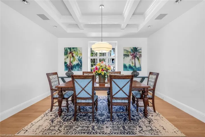 Dining room with light wood-style floors, beamed ceiling, coffered ceiling, and ornamental molding