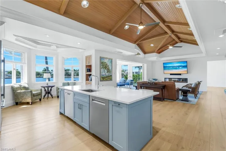 Kitchen with open floor plan, light wood finished floors, light stone countertops, recessed lighting, and a center island with sink