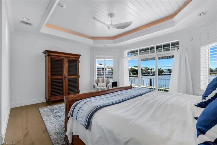 Bedroom with access to exterior, multiple windows, hardwood / wood-style floors, a raised ceiling, and ornamental molding