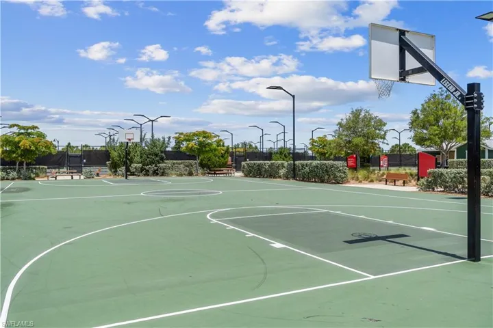 Outdoor basketball court with a green surface, white court lines, multiple basketball hoops, and perimeter lighting