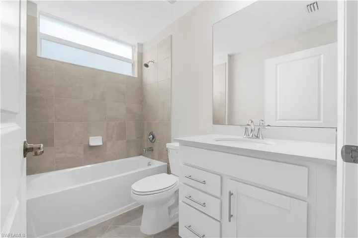 Modern bathroom with a white vanity, integrated sink, large wall-mounted mirror, and a combination tub/shower with tiled surround