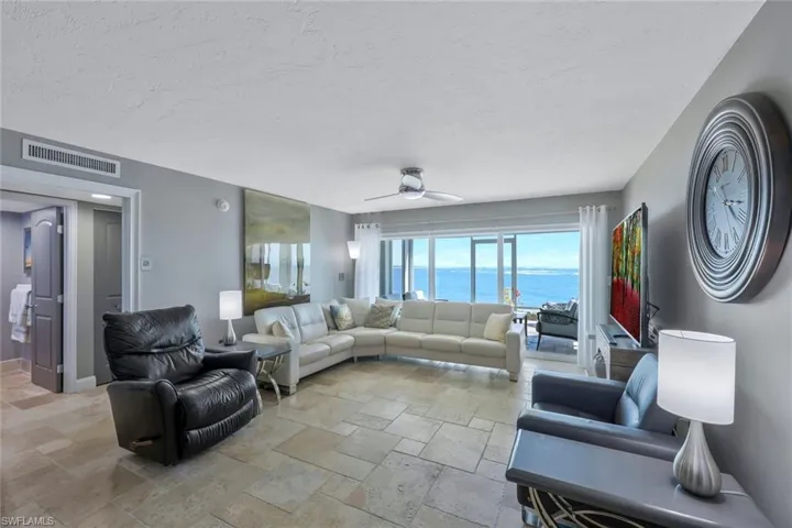 Living room with stone tile floors, baseboards, visible vents, ceiling fan, and a textured ceiling