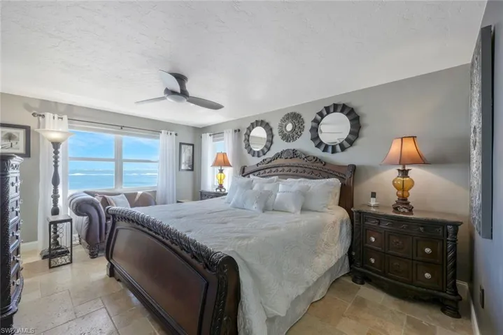 Bedroom featuring stone tile flooring, a textured ceiling, baseboards, and a ceiling fan