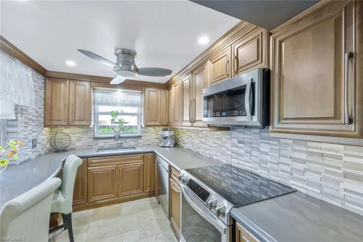 Kitchen with stone finish floor, a sink, backsplash, appliances with stainless steel finishes, and ceiling fan