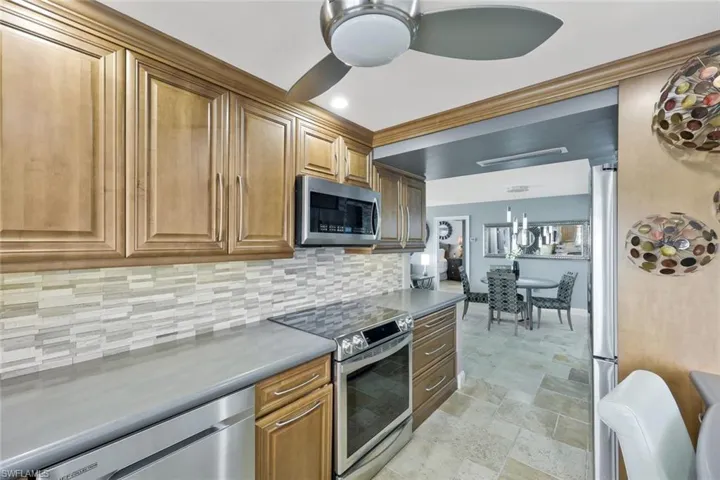 Kitchen with dark countertops, decorative backsplash, brown cabinetry, stainless steel appliances, and a ceiling fan