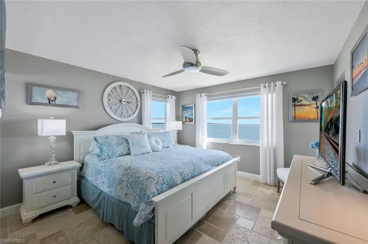 Bedroom featuring baseboards, a textured ceiling, stone tile floors, and ceiling fan