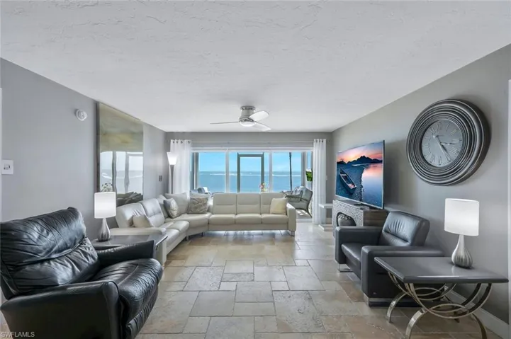 Living area featuring stone tile flooring, ceiling fan, a textured ceiling, and baseboards