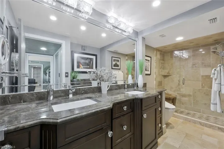 Full bath featuring stone tile floors, visible vents, a stall shower, and a sink