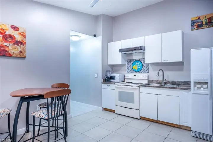 Kitchen featuring white appliances, sink, white cabinetry, and light tile floors
