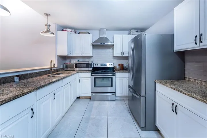Kitchen featuring stainless steel appliances, wall chimney exhaust hood, sink, tasteful backsplash, and light tile floors