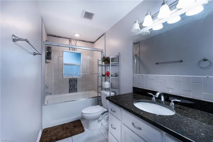 Full bathroom with shower / bath combination with glass door, tile floors, backsplash, large vanity, and toilet