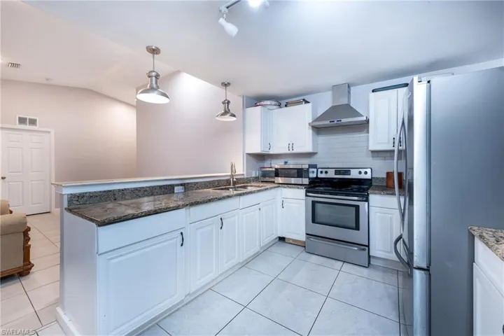 Kitchen with wall chimney range hood, hanging light fixtures, light tile floors, and appliances with stainless steel finishes